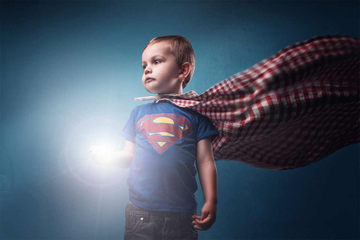 Photograph of a young boy in a Superman shirt with a cape made from a tablecloth