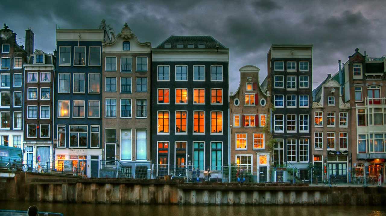 A row of houses with lit windows along an Amsterdam canal