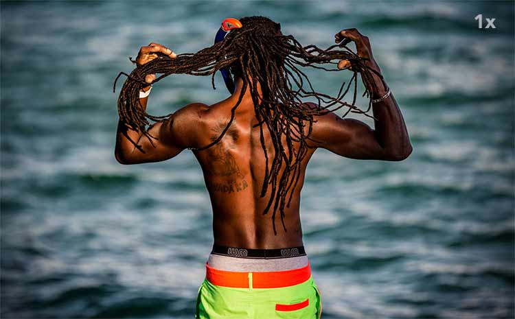 Photograph of a dreadlocked man from behind as he faces the ocean